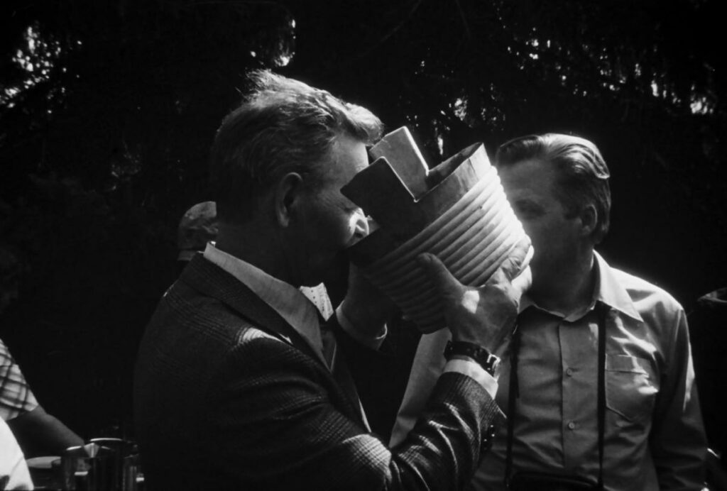 Mies juo puisesta haarikasta. Mustavalkoinen kuva.