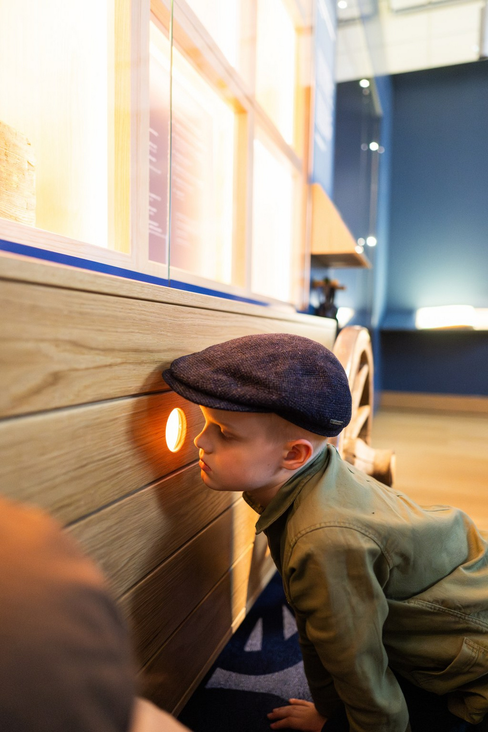 Lapsi hattu päässä katsoo näyttelyssä pienestä reiästä sisään.